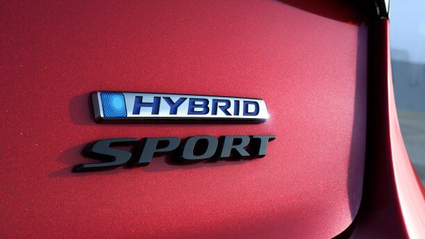 Gros plan des emblèmes « Hybrid » et « Sport » sur le coffre d’une Accord rouge.