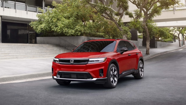 Vue latérale d’un Prologue rouge branché à un chargeur dans l’abri d’auto d’une maison moderne.