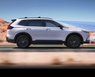 Vue latérale d’un CR-V blanc roulant sur une autoroute dans le désert.