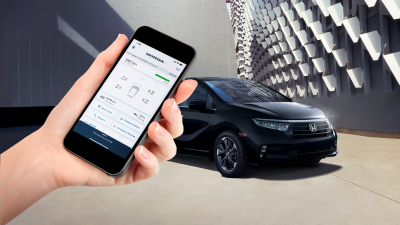 Une Odyssey noire stationnée devant un bâtiment d’architecture contemporaine. Une main au premier plan tient un téléphone intelligent affichant l’application HondaLink.
