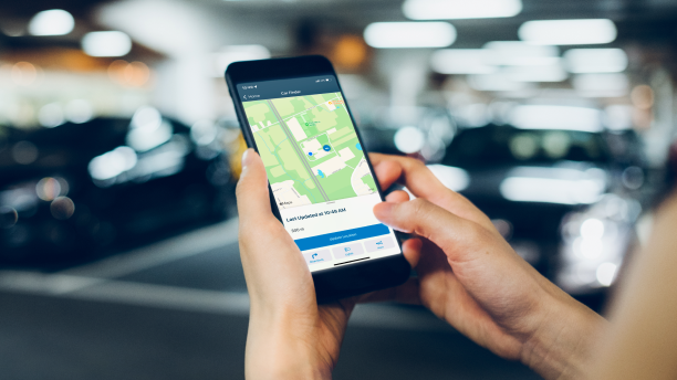 Gros plan des mains d’une personne qui utilise l’application HondaLink sur son téléphone dans un stationnement à étages. Accord grise stationnée en arrière-plan.