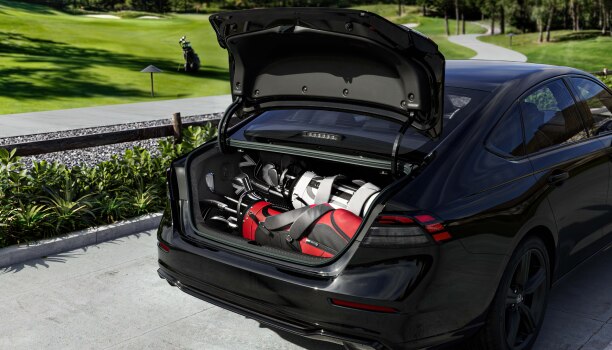 Wide view of the open trunk on a black Accord with two golf bags in it. 