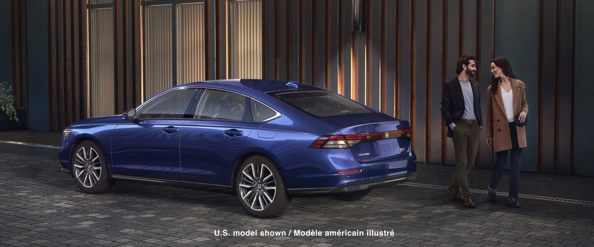 3/4 rear view of blue Accord parked outside of a trendy urban building. A well-dressed couple walks away from it. 