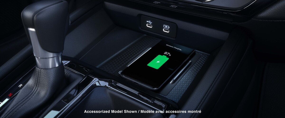 Gros plan d’un téléphone intelligent compatible qui se recharge sans fil sur le tapis de recharge devant le levier de vitesses.