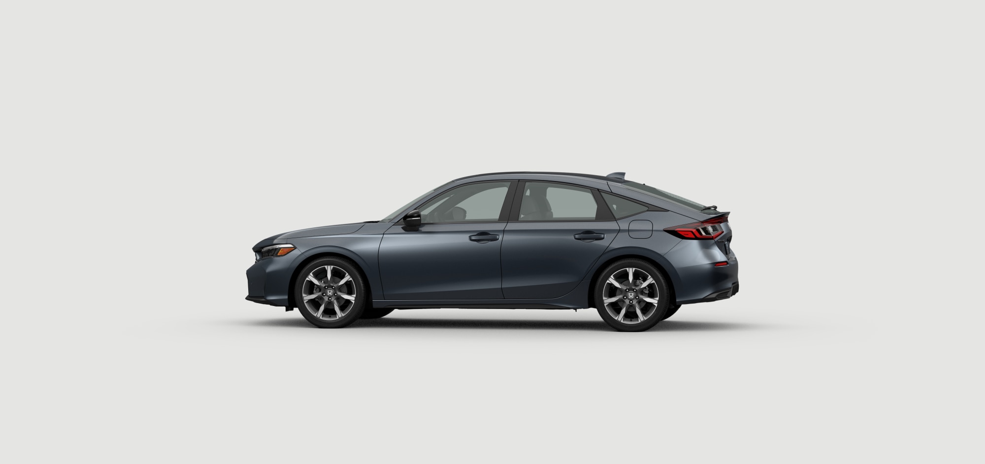 Vue latérale du côté conducteur de la Civic à hayon Sport Hybride Touring 2025 de couleur gris urbain nacré fond blanc. 