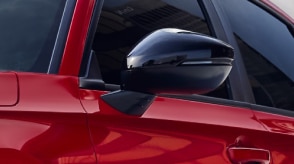 Gros plan d’un rétroviseur extérieur noir sur une Civic berline rouge.