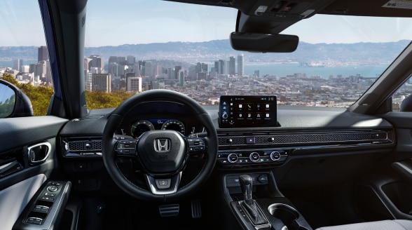 Panoramic view through the windshield, overlooking a waterfront cityscape. 
