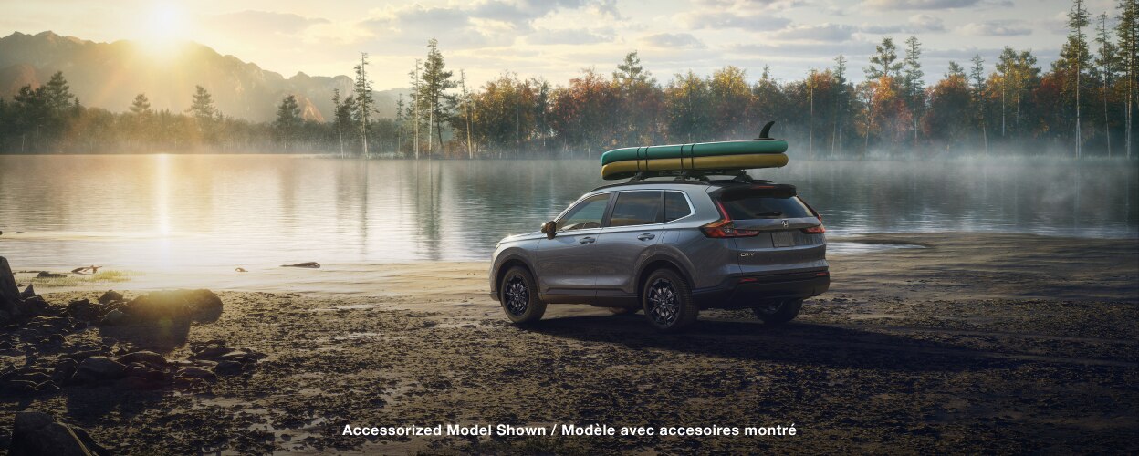 3/4 rear sideview of grey CR-V, with two paddle boards on the roof racks, parked on a lake shoreline on a dewy morning.