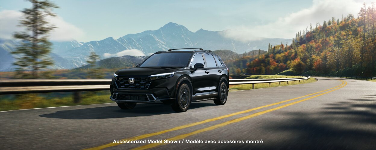 3/4 front view of black CR-V driving on a winding forest highway with fall-coloured trees and mountain range as backdrop. 