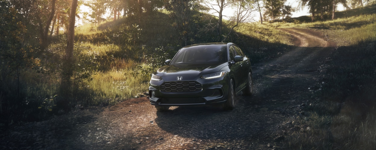 Vue 3/4 avant d’un HR-V noir roulant vers la caméra sur une route de terre en campagne.