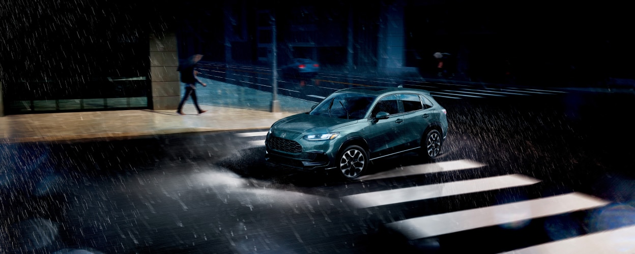 Vue 3/4 latérale d’un HR-V forêt nordique nacrée roulant sous la pluie en ville.
