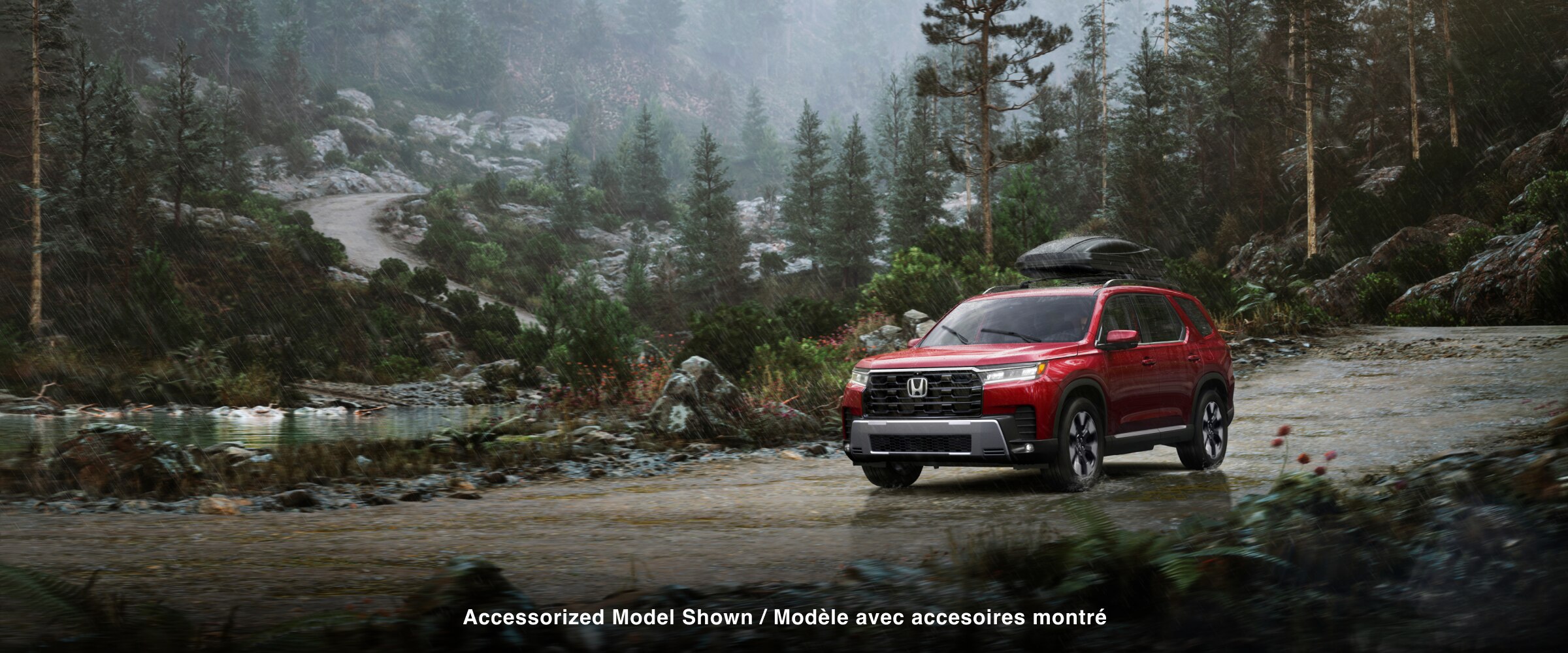 3/4 front side view of a red Pilot driving on a dirt road through a forest in the rain, with a cargo box mounted on its roof. 
