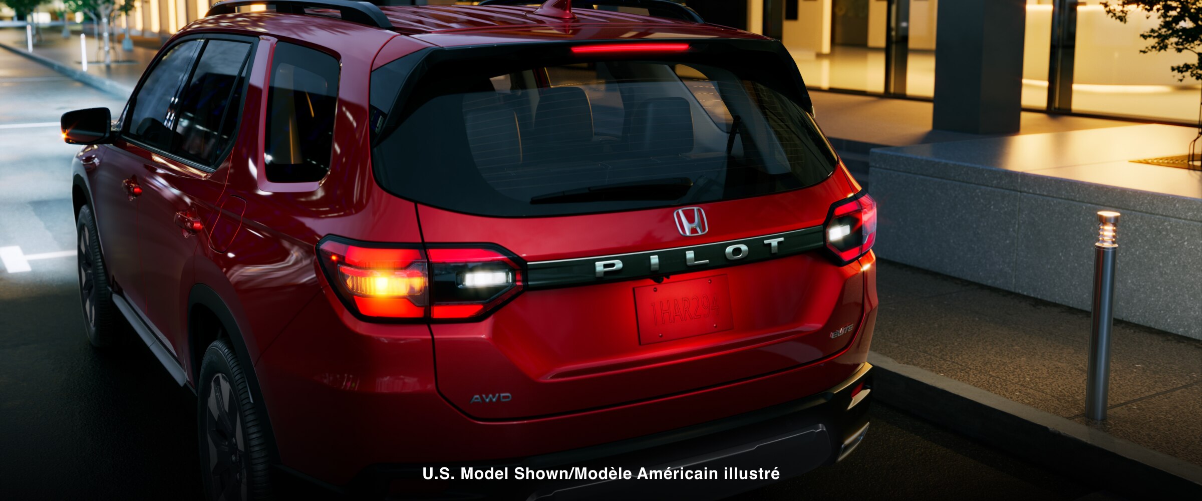 3/4 rear side view of a red Pilot parked on a city street at night, rear headlights glowing. 