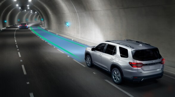 3/4 rear view of a silver Pilot driving through a tunnel with blue and green sensors monitoring the lane ahead.