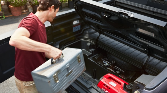 Homme chargeant un coffre à outils dans le coffre intégré In-Bed Trunk verrouillable.