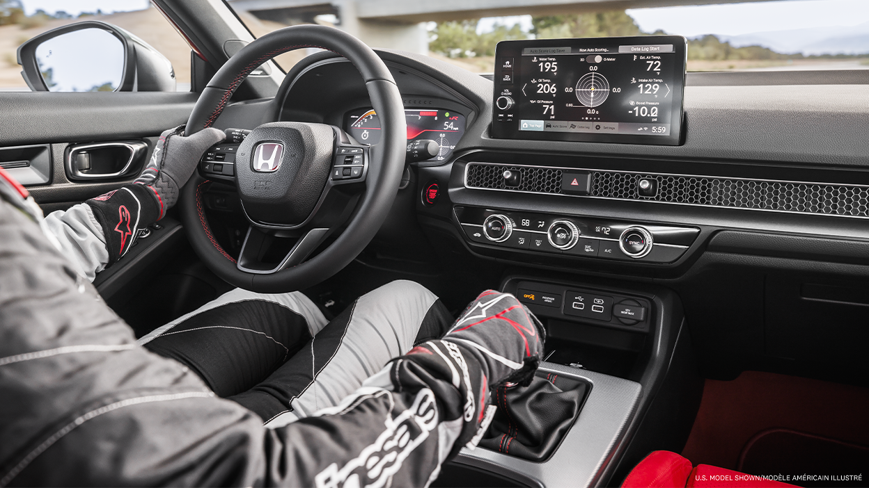 Vue intérieure d’un pilote tenant le volant, de l’habitacle de la Type R et des renseignements du système LogR à l’écran tactile.