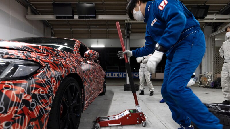 A Type R, with a funky red paint job with white Type R monograms, in a garage about to get lifted with a jack.