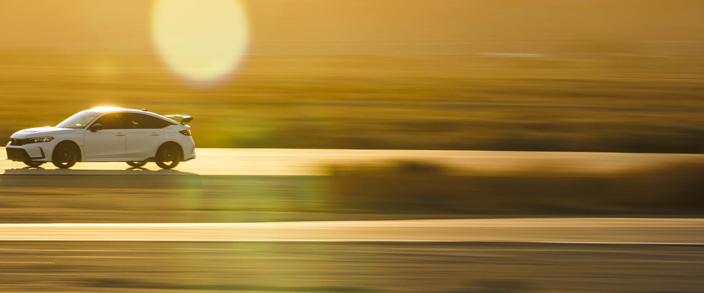 Plan d’ensemble et vue latérale d’une Type R blanche conduite sur une autoroute au coucher du soleil dans le désert. La partie avant est plus visible.
