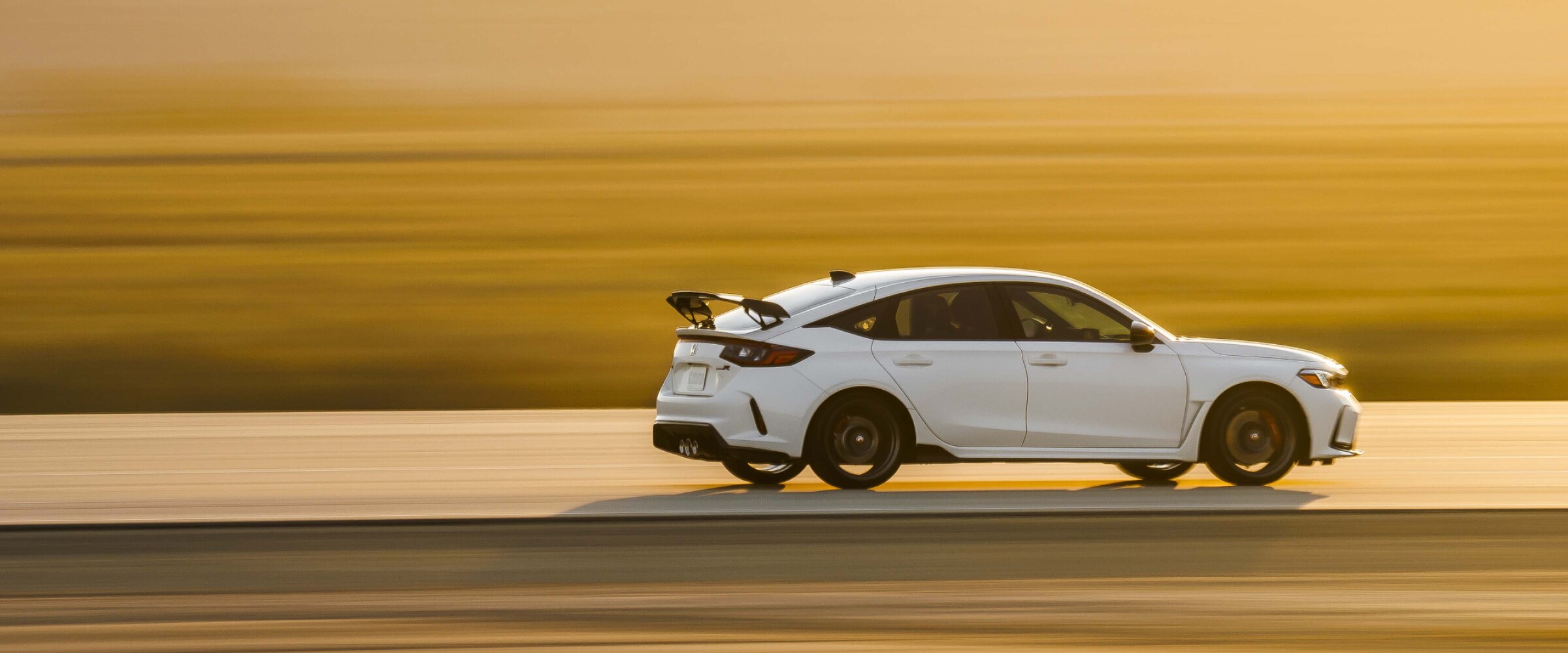 Plan d’ensemble et vue latérale d’une Type R blanche conduite sur une autoroute au coucher du soleil dans le désert. La partie arrière est plus visible.