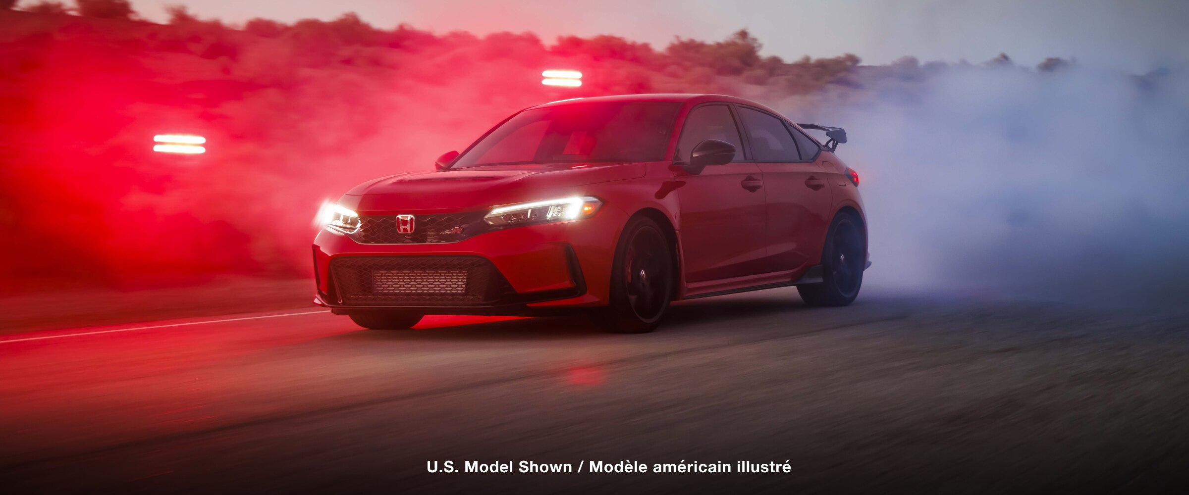 3/4 front view of a red Type R burning rubber on a desert road at dusk. 