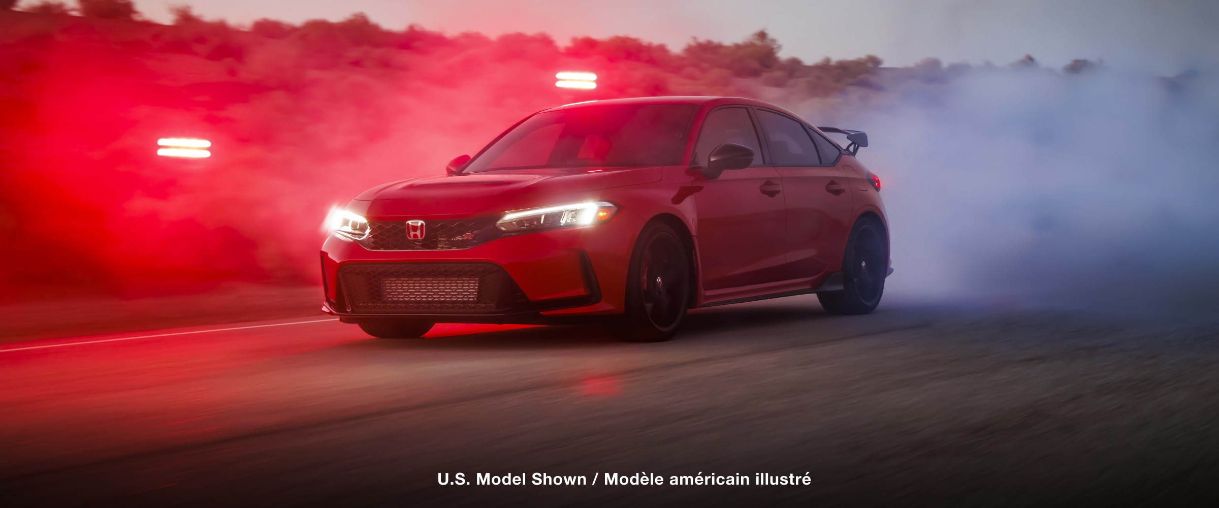 3/4 front view of a red Type R burning rubber on a desert road at dusk.