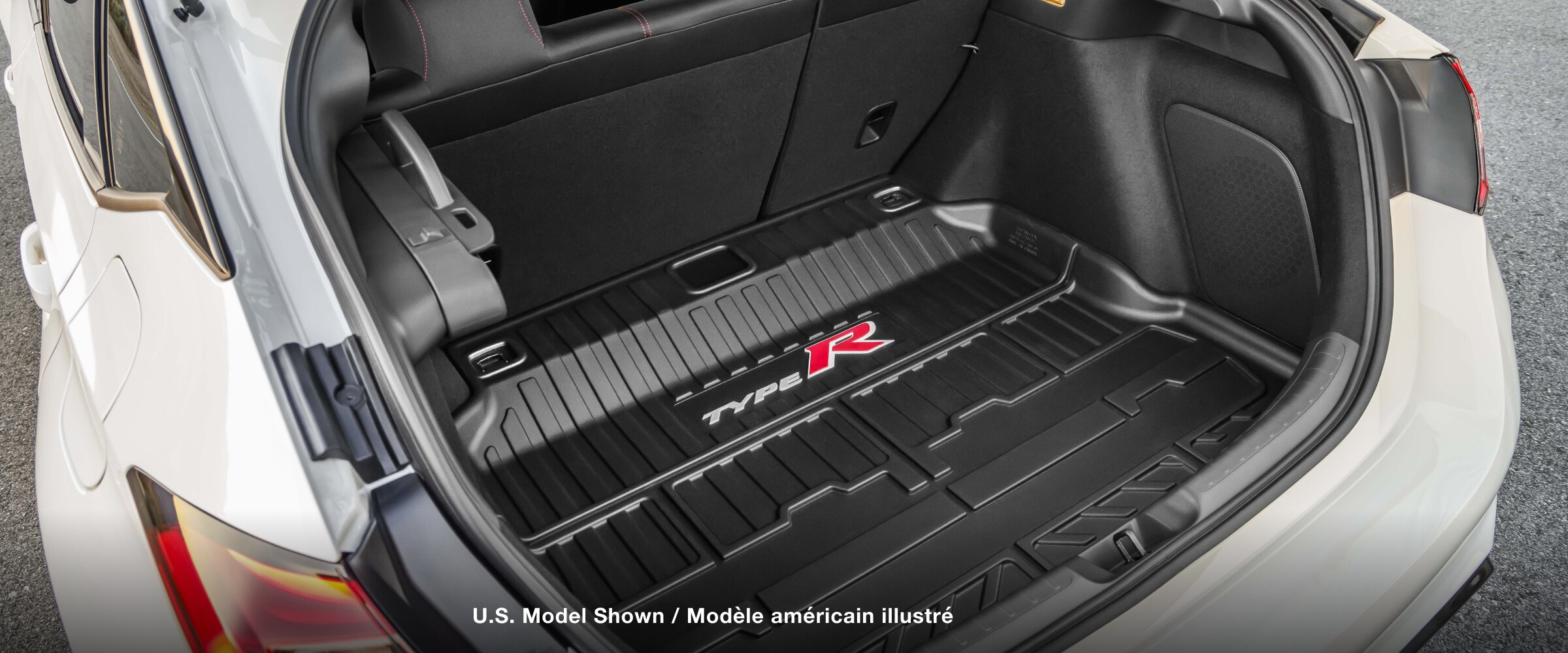 Closeup of an open trunk on a white Type R, showing the speakers and the custom-fit “Type R” branded rubber trunk mat. 