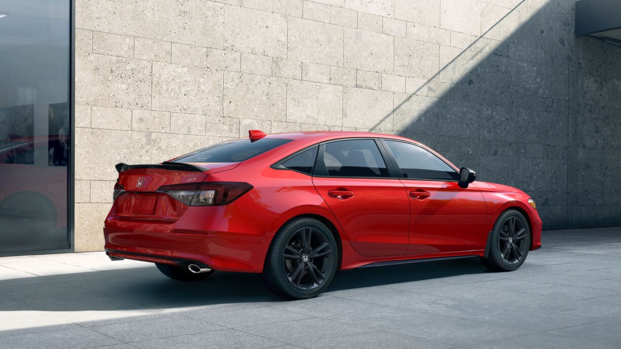 3/4 rear view of a red Civic parked in an urban setting. 