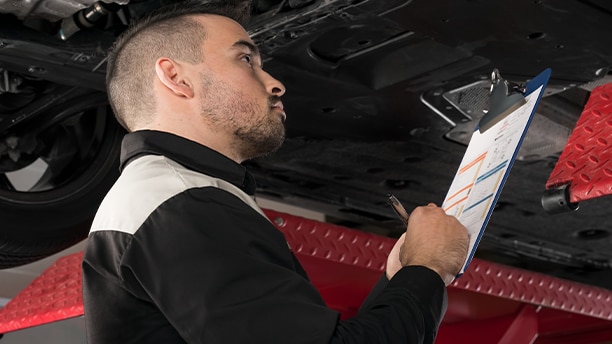 Un technicien Honda regardant sous un véhicule Honda et prenant des notes sur un presse-papiers.