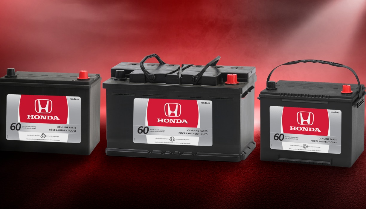 Trois batteries Honda côte à côte sur un fond rouge flou.